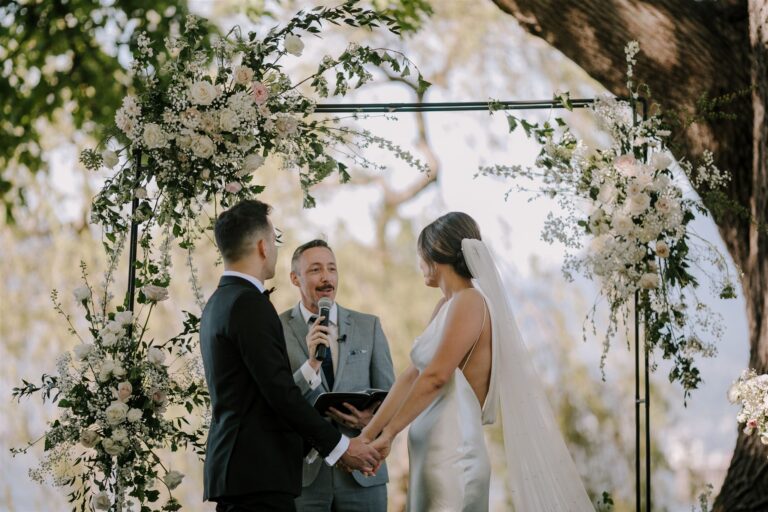 A couple exchanging vows beneath a garden arch