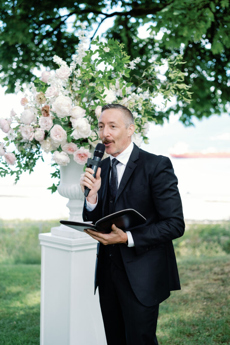 Jonathan Evans speaking beneath a floral arch by the water