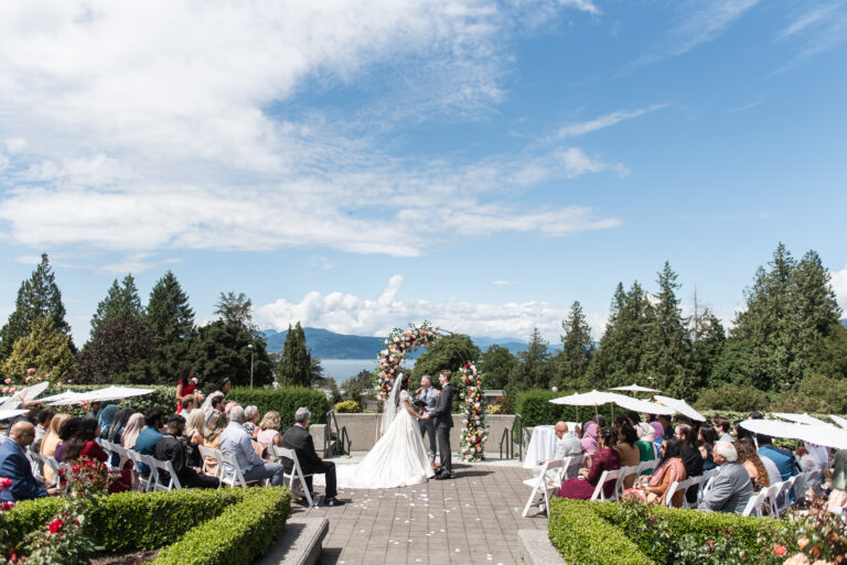 A couple beneath a floral arch with a waterfront view behind