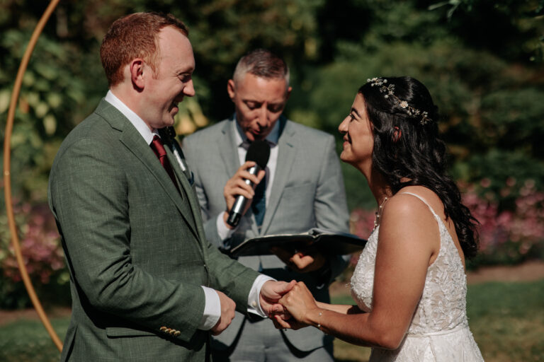 A couple holding hands during their vows, the officiant just behind