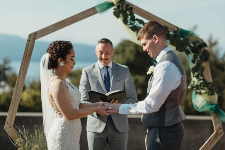 Jonathan Evans smiling between the couple as they exchange rings
