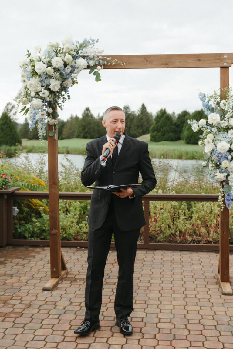 Jonathan Evans officiating an outdoor ceremony beside a floral arch