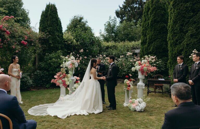 Nick and Lindsay holding hands in a garden ceremony as Jonathan Evans officiates